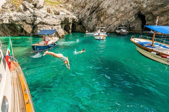 Swimmers diving from a boat into clear green water beside sea caves near Capri